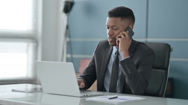 Afrikansk affärsman Talar på smartphone när du använder laptop i Office — Stockvideo