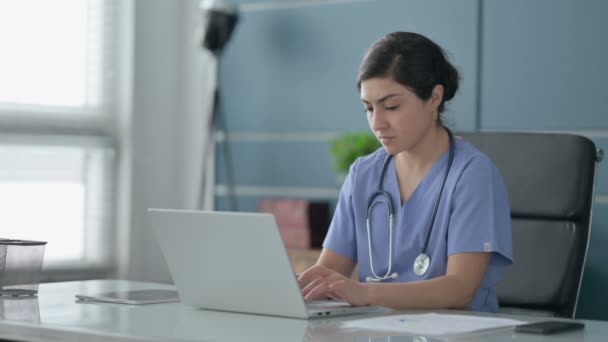 Médico femenino indio pensando mientras trabaja en el ordenador portátil en la oficina — Vídeos de Stock