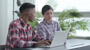 Belgelerle birlikte dizüstü bilgisayarda çalışan Afrikalı Adam ve Hintli Kadın