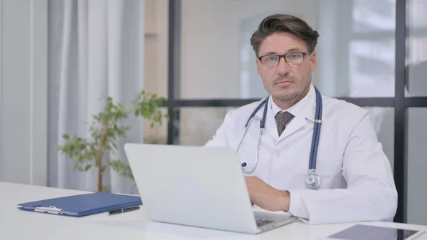 Dokter met laptop kijkend naar de camera in de kliniek — Stockfoto