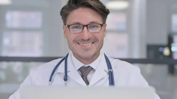 Primer plano del médico con el ordenador portátil sonriendo a la cámara — Foto de Stock