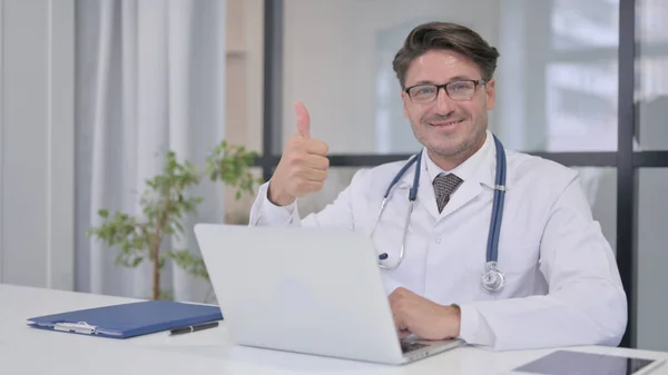 Médico con Laptop mostrando pulgares hacia arriba en la clínica — Foto de Stock