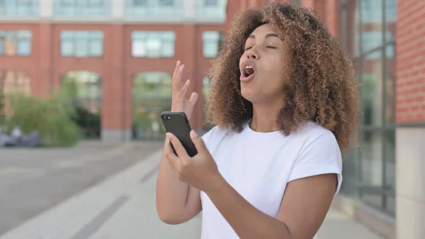 Młoda Afrykanka reaguje na stratę na smartfonie, Na zewnątrz — Zdjęcie stockowe