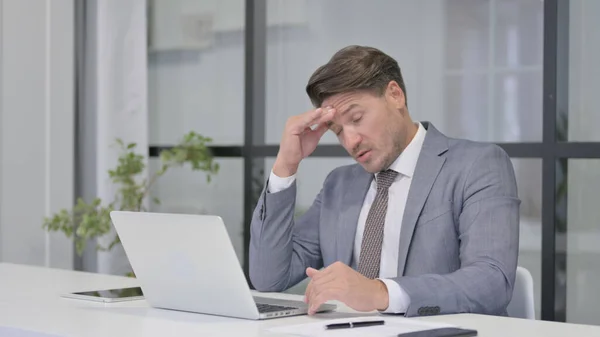 Un bărbat de vârstă mijlocie suferă de dureri de cap în timp ce lucrează la laptop — Fotografie, imagine de stoc