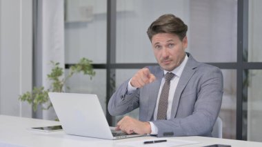 Ofiste dizüstü bilgisayar kullanırken Orta yaşlı adam kamerayı işaret ediyor