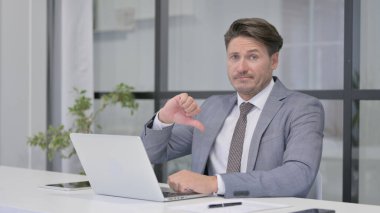 İşyerinde dizüstü bilgisayar kullanırken Orta Yaşlı Adam İşaret İşaretini Gösteriyor