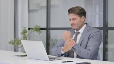 Dizüstü bilgisayar kullanırken bilek ağrısı çeken orta yaşlı bir adam.