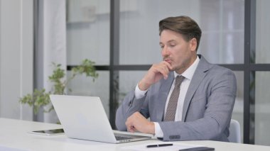 Ofisteki dizüstü bilgisayarda çalışırken düşünen orta yaşlı adam