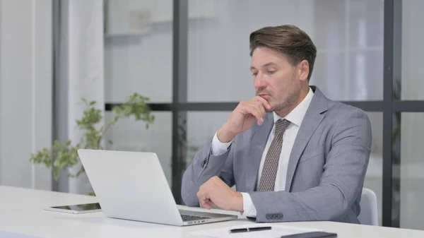 Medelålders man tänker medan du arbetar på laptop i Office — Stockfoto