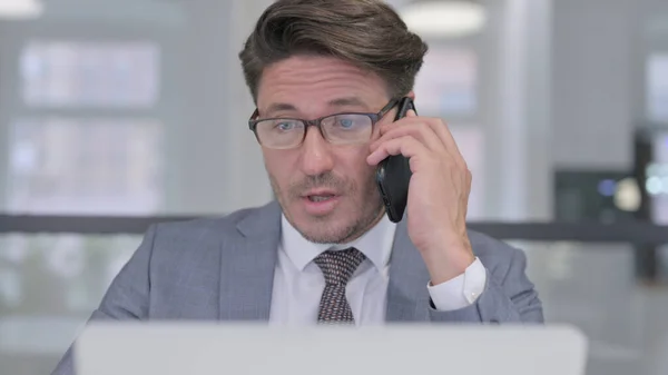 Primer plano del hombre de negocios de mediana edad con el ordenador portátil hablando por teléfono —  Fotos de Stock