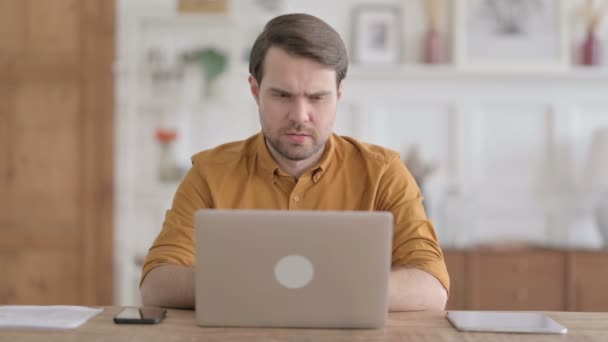 Молодой человек думает во время работы над ноутбуком в офисе — стоковое видео
