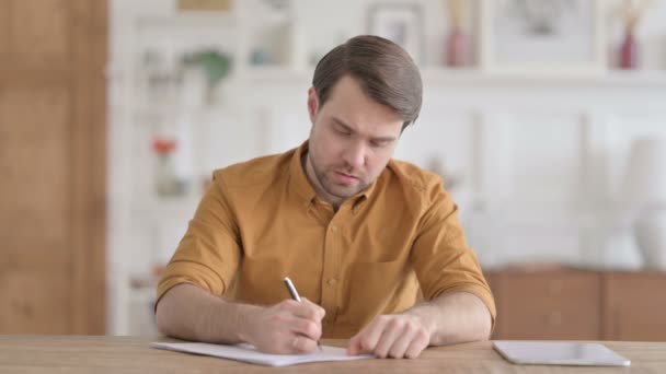 Jeune homme réfléchissant tout en écrivant sur le papier au bureau — Video