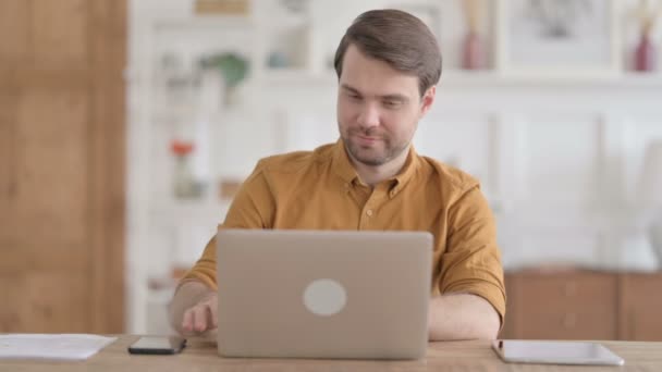Молодий чоловік розмовляє на відеозв'язку на ноутбуці в офісі — стокове відео