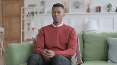 Kanepede oturan Afrikalı adam öksürüyor. 