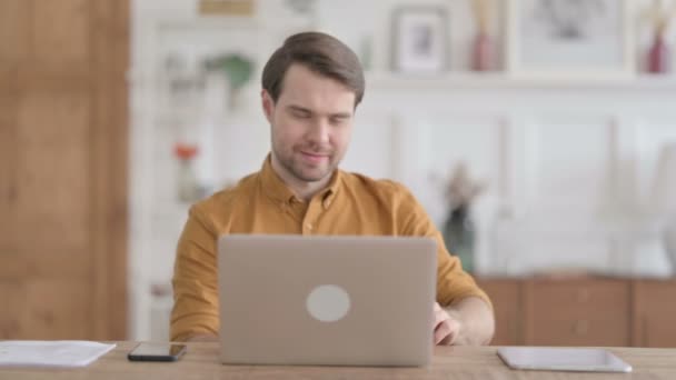 Молодий чоловік, який знову страждає, користуючись ноутбуком у офісі — стокове відео