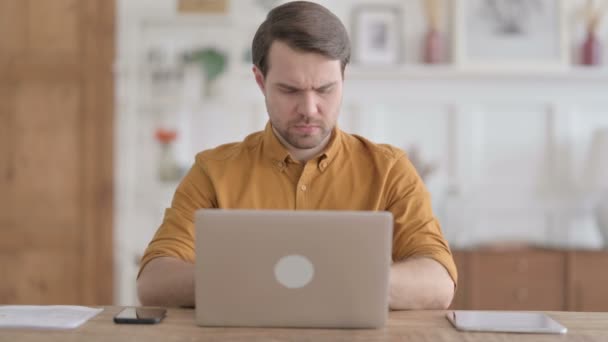 Молодий чоловік, який відчуває запальну біль, користуючись ноутбуком у офісі — стокове відео