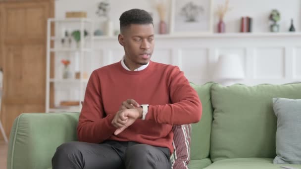 Africain homme en attente tout en vérifiant regarder sur canapé — Video