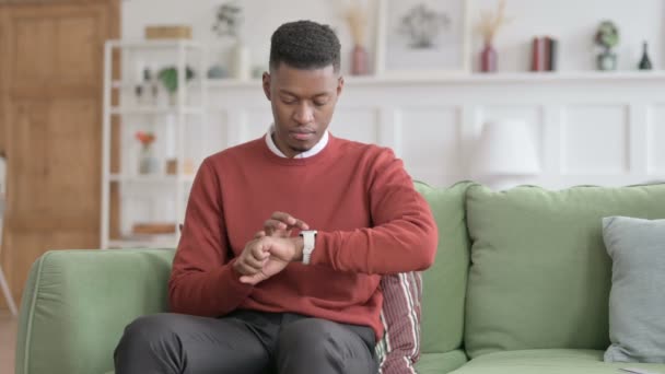 Αφρικανικός άνθρωπος χρησιμοποιώντας Smart Watch, ενώ κάθεται στον καναπέ — Αρχείο Βίντεο
