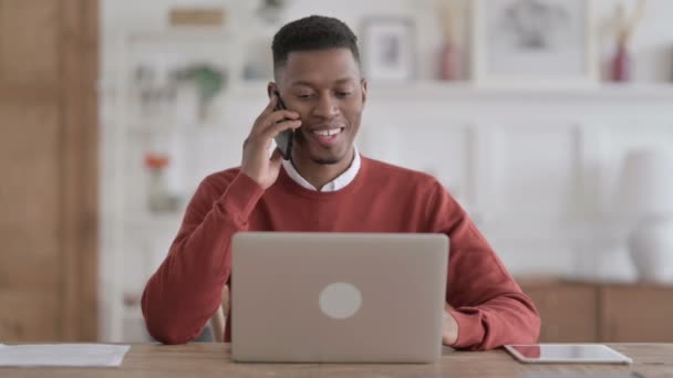 Africain parler au téléphone tout en utilisant un ordinateur portable dans le bureau — Video