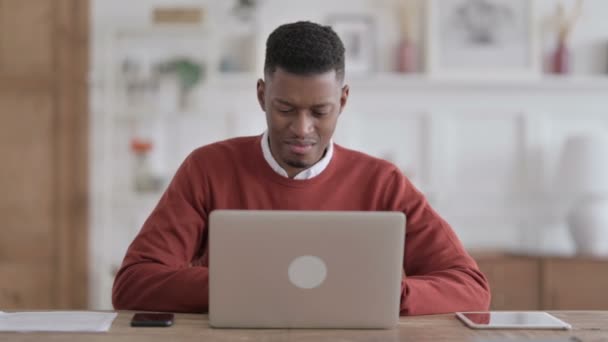 Африканський чоловік повертається до болю, користуючись ноутбуком у офісі — стокове відео