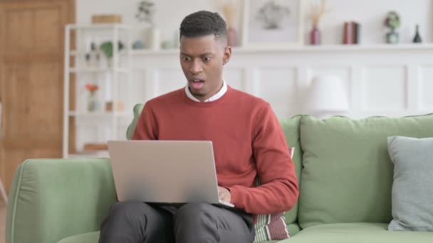 Afrikansk man med bärbar dator som reagerar på förlust på soffan — Stockvideo