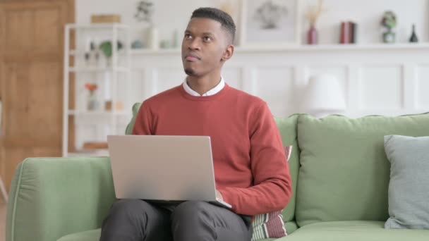 Afrikansk man tänker medan du arbetar på laptop på soffan — Stockvideo