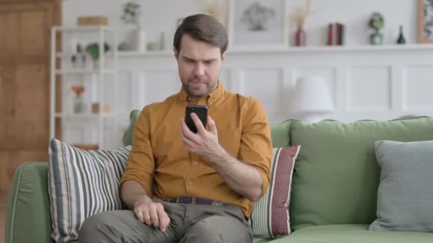 Młody człowiek traci na smartfonie w domu — Wideo stockowe