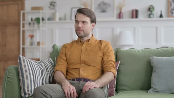 Привлекательный молодой человек сидит на диване — стоковое видео