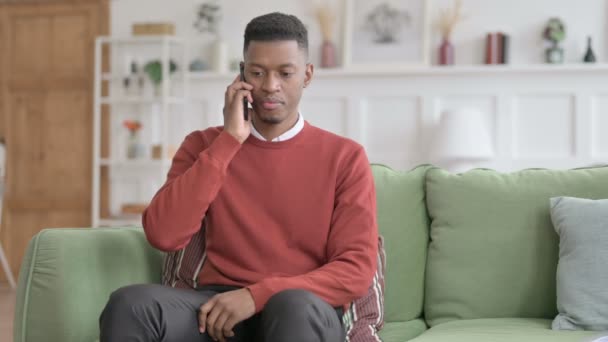 Arg afrikansk man pratar i telefon på soffan — Stockvideo
