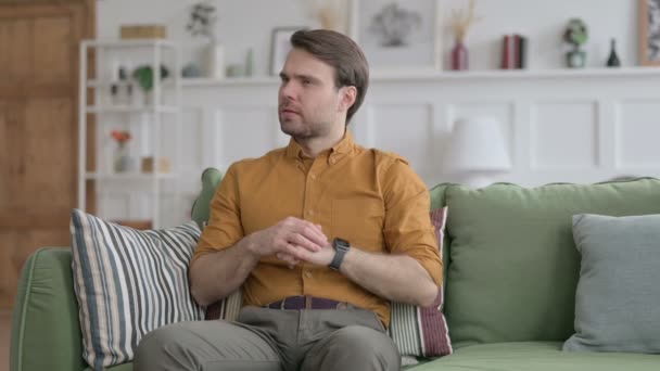 Joven hombre esperando mientras revisa reloj en sofá — Vídeos de Stock