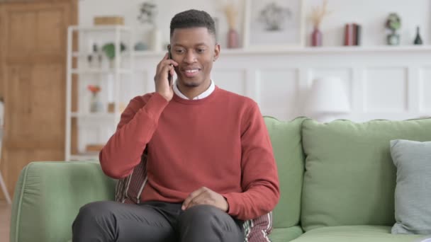 Afrikansk man talar i telefon på soffan — Stockvideo