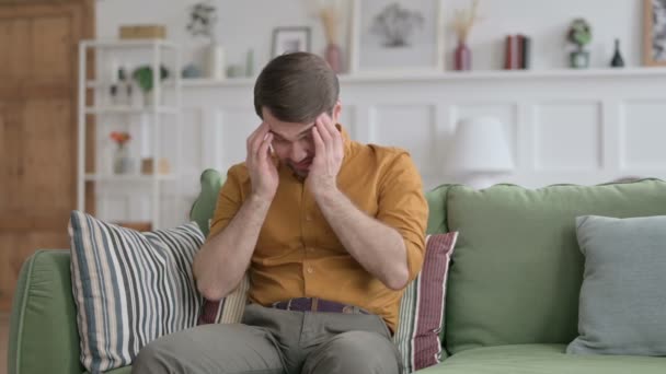 Junger Mann sitzt mit Kopfschmerzen auf Sofa — Stockvideo
