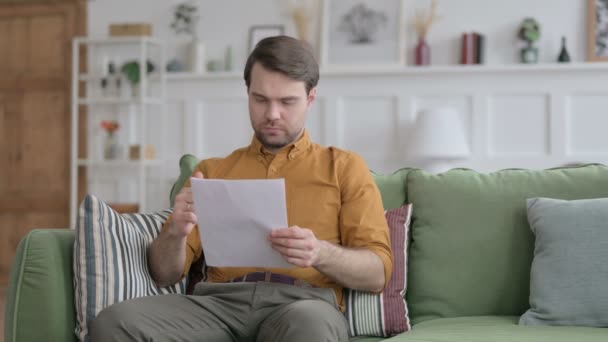 Joven leyendo documentos en el sofá — Vídeos de Stock