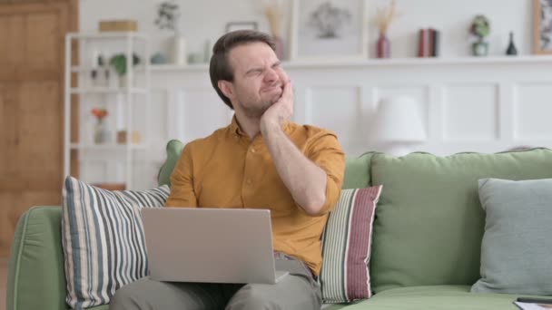 Молодой человек с ноутбуком с болями в шее на диване — стоковое видео