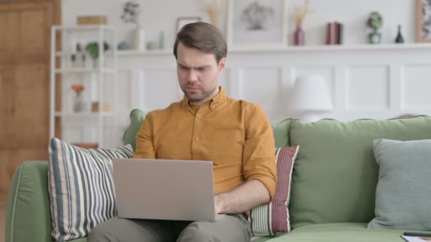 Молодой человек с ноутбуком с болями в шее на диване — стоковое видео