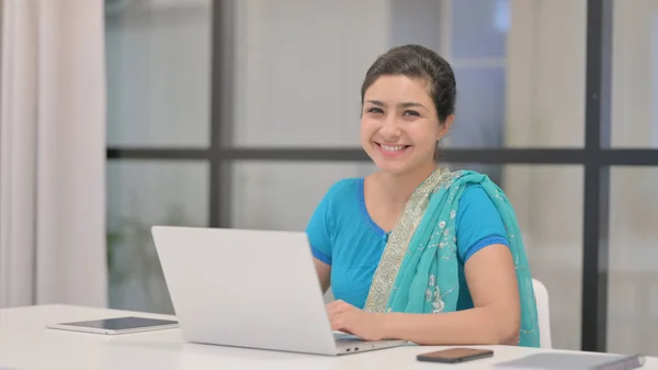 Индийская женщина улыбается перед камерой, пользуясь вершиной в офисе — стоковое фото