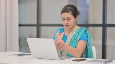 Ofiste dizüstü bilgisayar kullanırken bilek ağrısı çeken Hintli kadın.