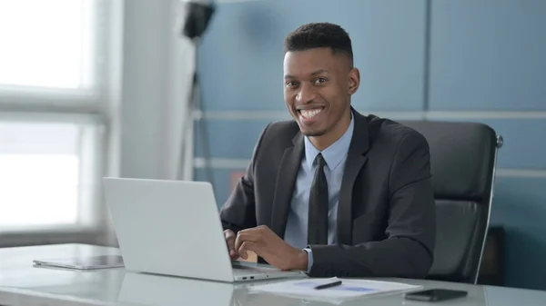 Afrikansk affärsman ler mot kameran när du använder laptop i Office — Stockfoto