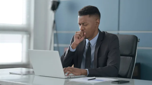 Afrikanischer Geschäftsmann hustet, während er Laptop im Büro benutzt — Stockfoto