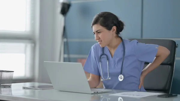 Indiase vrouwelijke arts met rugpijn tijdens het gebruik van laptop in Office — Stockfoto