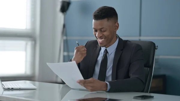 Afrikansk affärsman firar framgång när han läser dokument på kontoret — Stockfoto