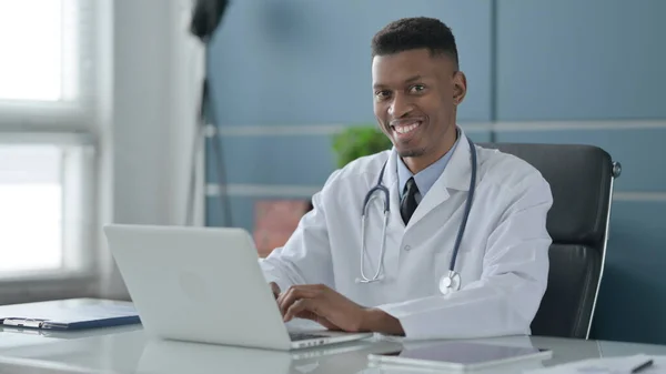 Afrikanska doktor ler mot kameran när du använder laptop i Office — Stockfoto