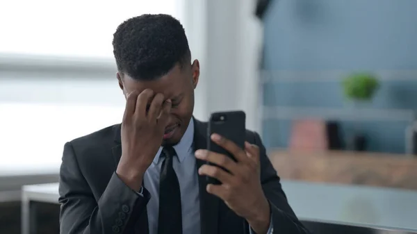 Afrikanischer Geschäftsmann reagiert auf Verlust mit Smartphone — Stockfoto