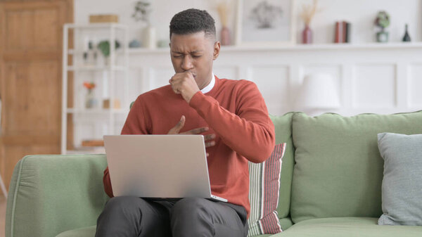 African Man with Laptop Coughing on Sofa