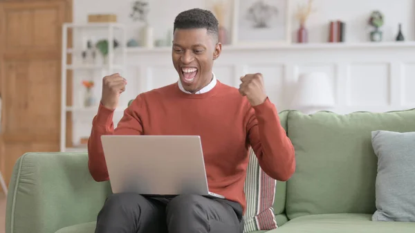Afrikai férfi laptoppal ünnepli a sikert a kanapén — Stock Fotó