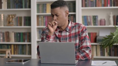 Ofiste dizüstü bilgisayar kullanırken Afrikalı Adam öksürüyor 