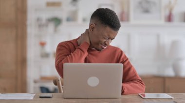 Ofiste dizüstü bilgisayar kullanırken boynu ağrıyan Afrikalı adam