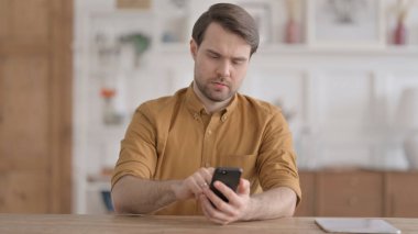 Ofiste akıllı telefon kullanan çekici genç adam.