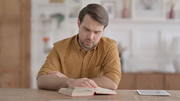 Jongeman die het boek leest terwijl hij op kantoor zit — Stockfoto