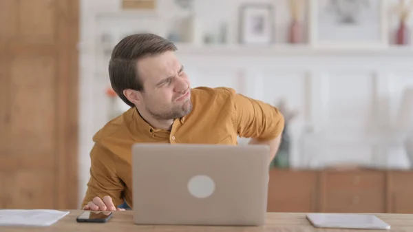 Hombre joven que tiene dolor de espalda mientras usa el ordenador portátil en la oficina — Foto de Stock
